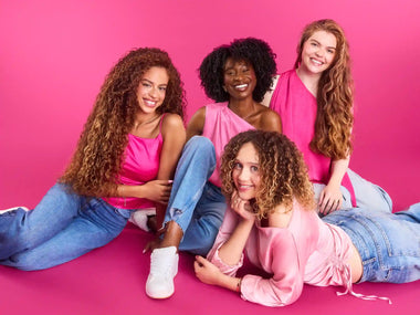 4 women with textured hair on a pink background